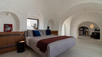 Un dormitorio amplio con una cama grande, cabecera de madera y vista a través de un ventanal arqueado.