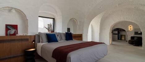 Un dormitorio amplio con una cama grande, cabecera de madera y vista a través de un ventanal arqueado.