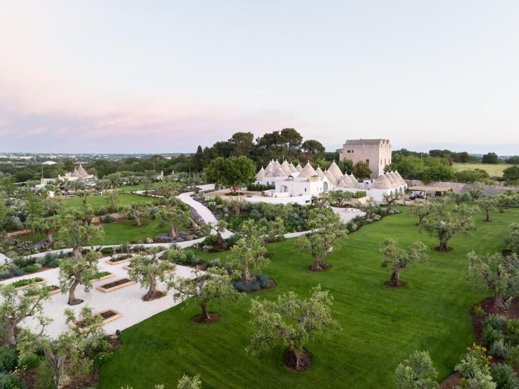 A landscaped garden with a variety of trees and a large building with multiple conical structures.