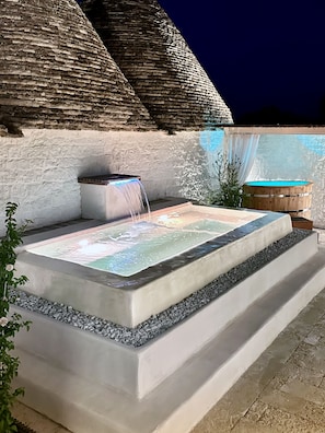 A hot tub with a waterfall feature, surrounded by a stone wall and a wooden barrel.
