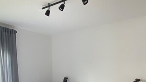 En säng för en person med en träram, vita sängkläder och en sänggavel. Det finns två sängbord, varav det ena har en lampa, och ett fönster med gardiner.