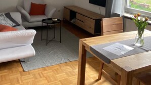 Ett modernt vardagsrum med en soffa, ett soffbord i trä, en tv och ett matbord med en vas med blommor.