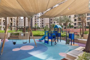 A playground with swings, slides, and climbing structures, surrounded by palm trees and a covered area. - StayShort | Stylish 1BR Apartment | Near Burj Al Arab | Family-Friendly | Sleeps 4 (Dubai)