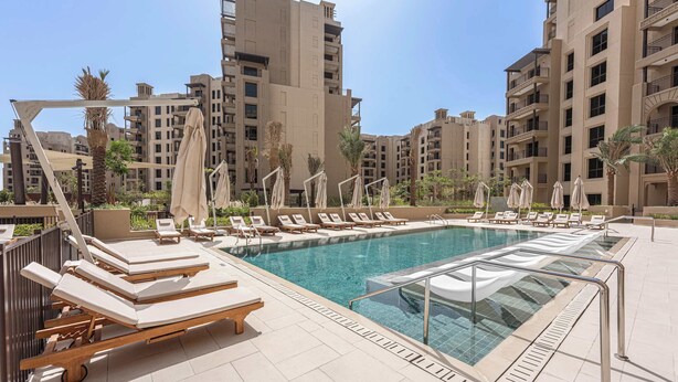 A rooftop swimming pool with sun loungers and umbrellas, surrounded by high-rise buildings. - StayShort | Stylish 1BR Apartment | Near Burj Al Arab | Family-Friendly | Sleeps 4 (Dubai)