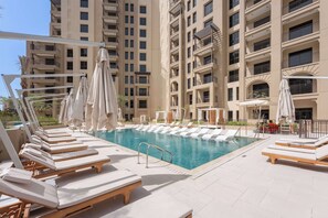A rooftop swimming pool with sun loungers and umbrellas, surrounded by a high-rise building with balconies. - StayShort | Stylish 1BR Apartment | Near Burj Al Arab | Family-Friendly | Sleeps 4 (Dubai)
