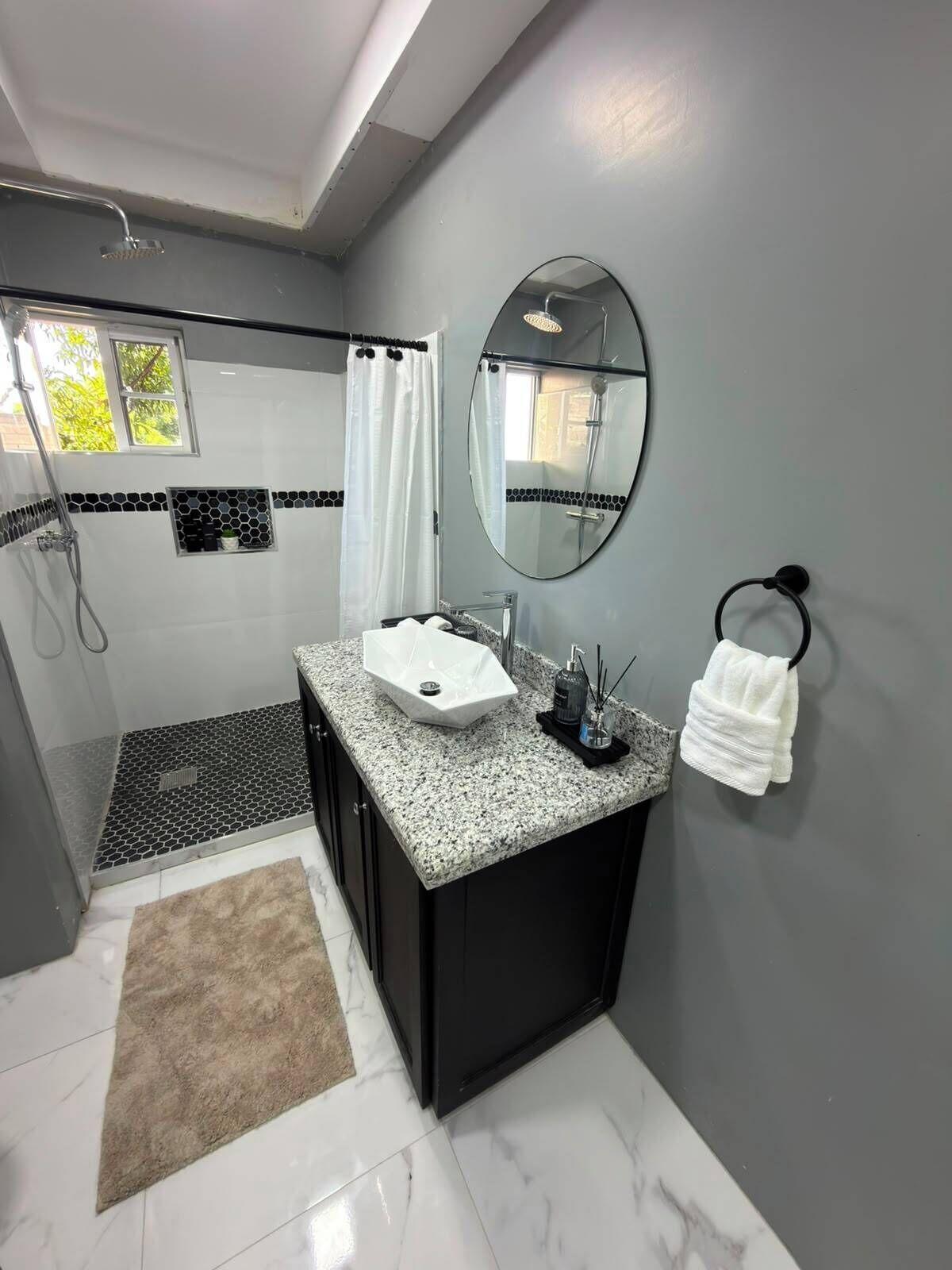Une salle de bain moderne avec un comptoir en granit, un lavabo blanc, un grand miroir et un porte-serviettes.