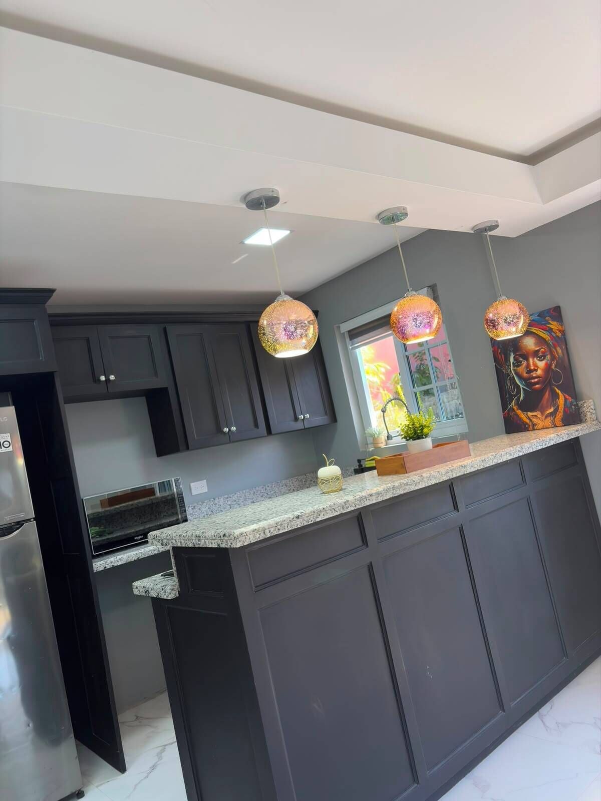 Une cuisine moderne avec des meubles de couleur sombre, un plan de travail en granit et des luminaires suspendus.