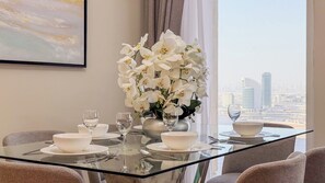 A dining table set with white bowls, glasses, and a vase of white flowers, with a cityscape view through a window. - Harbour Gate Residences - Creek Harbour (Dubai)