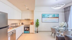 A modern kitchen with a stove, oven, and dishwasher, a dining area with a glass table and chairs, and a painting on the wall. - Harbour Gate Residences - Creek Harbour (Dubai)
