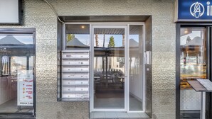 Une entrée d’immeuble avec une porte en verre, une boîte aux lettres en métal et un panneau indicateur.