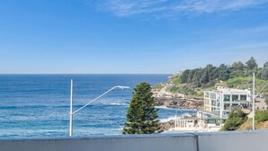 Une vue sur la côte, avec un ciel dégagé, un bâtiment portant une enseigne indiquant « SANDCREEK CLUB », et une côte rocheuse.