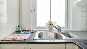 Une cuisine avec une fenêtre, un évier et un plan de travail agrémenté d’une plante et de quelques aliments.