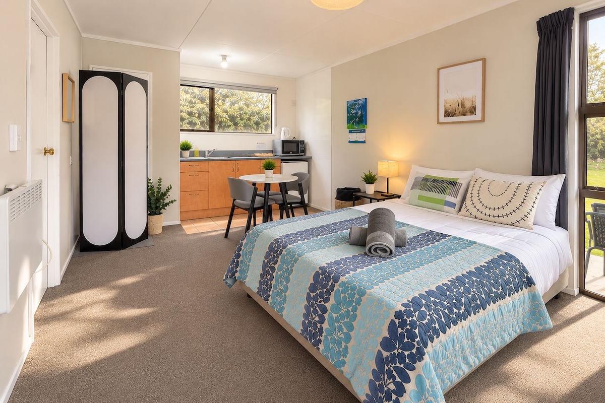 A bedroom with a bed, a bedside table, a lamp, and a window with curtains.