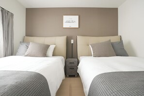 Habitación de hotel con dos camas, una mesita de noche, un enchufe y un cuadro en la pared.