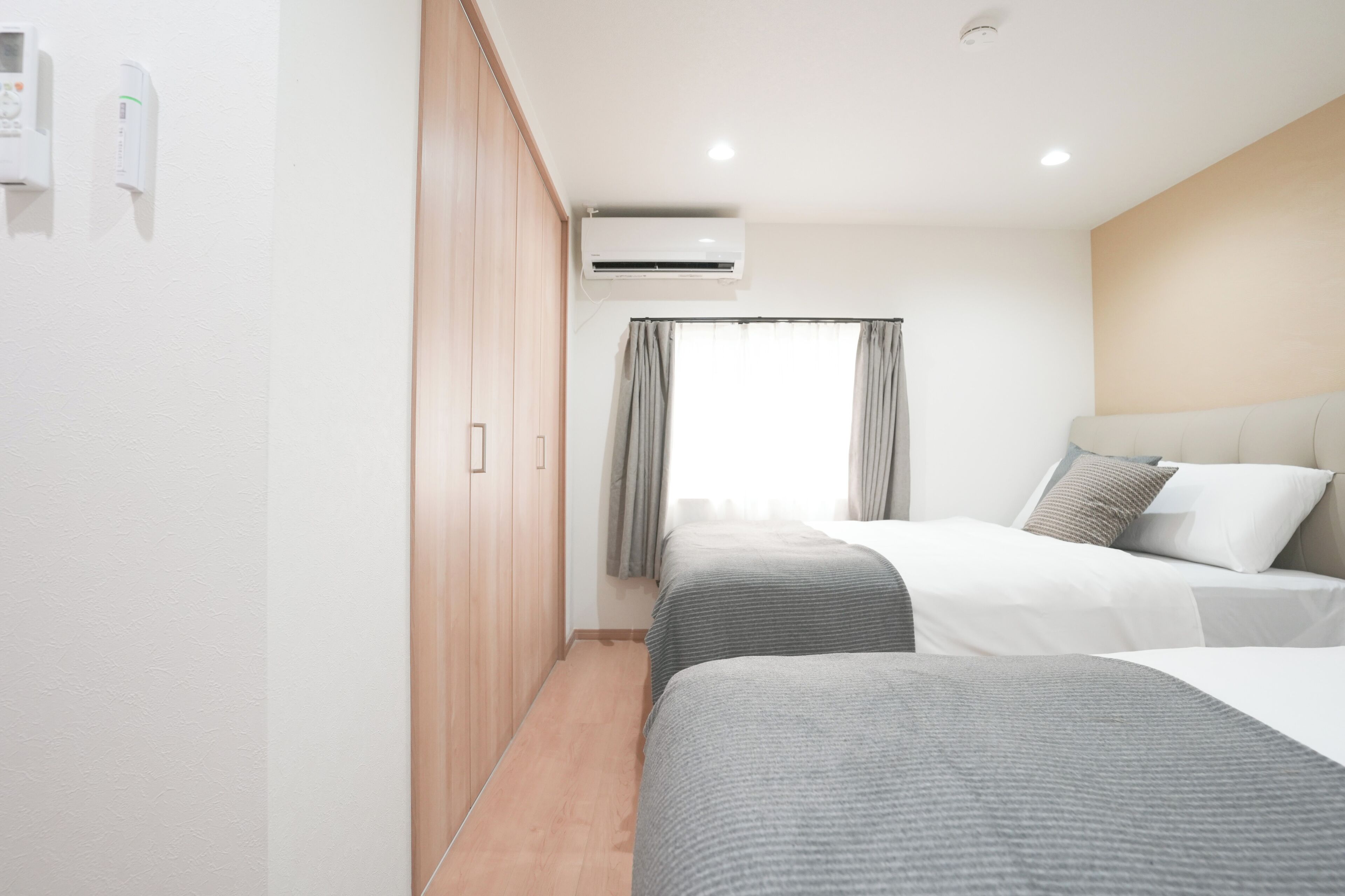 Una habitación de hotel con dos camas, un armario, aire acondicionado y una ventana con cortinas.
