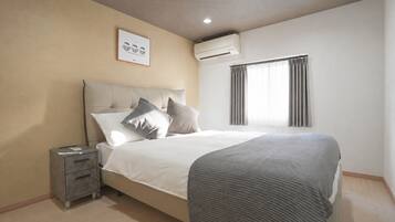 A bedroom with a bed, bedside tables, an air conditioning unit, a window with curtains, and a framed picture on the wall.