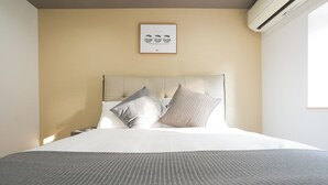 A neatly made bed with a striped bedspread and two pillows, a framed picture on the wall, and an air conditioning unit. - b&Tsutenkaku3 (Osaka Naniwa-ku)