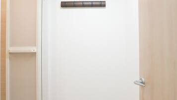 A room with a wooden floor, a white door, and a white wall with a light switch and a thermostat.