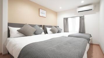 A hotel room with two beds, a framed picture on the wall, and an air conditioning unit.