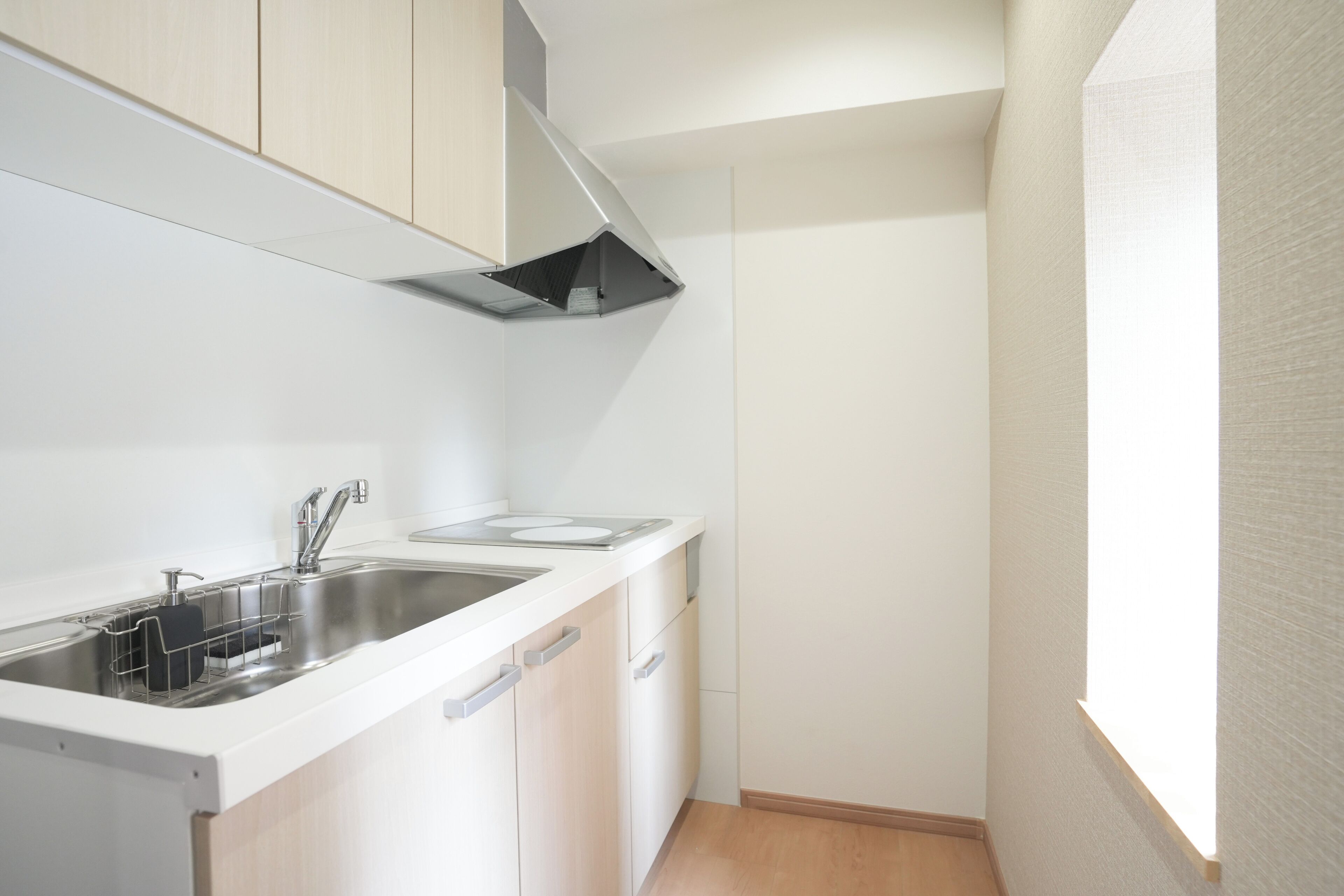 A compact kitchen with white cabinetry, a stainless steel sink, and a black range hood.