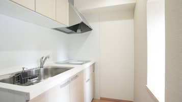 A compact kitchen with white cabinetry, a stainless steel sink, and a black range hood.