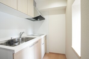 Una cocina compacta con muebles blancos, un lavamanos de acero inoxidable y una campana extractora negra.