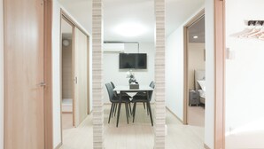 A modern interior with a dining area, a flat-screen TV mounted on the wall, and a hallway leading to a bedroom. - b&Tsutenkaku3 (Osaka Naniwa-ku)