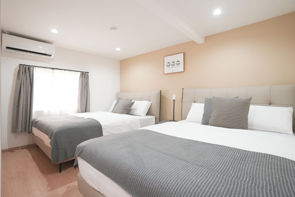 Habitación de hotel con dos camas, una ventana con cortinas, un equipo de aire acondicionado y una obra de arte colgada en la pared.
