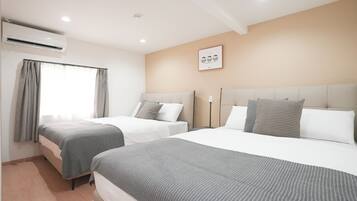 A hotel room with two beds, a window with curtains, an air conditioning unit, and a wall-mounted artwork.