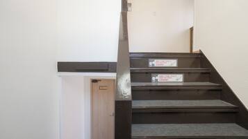 A staircase with a wooden door at the bottom, a sign with Japanese text, and a wall with a light switch.