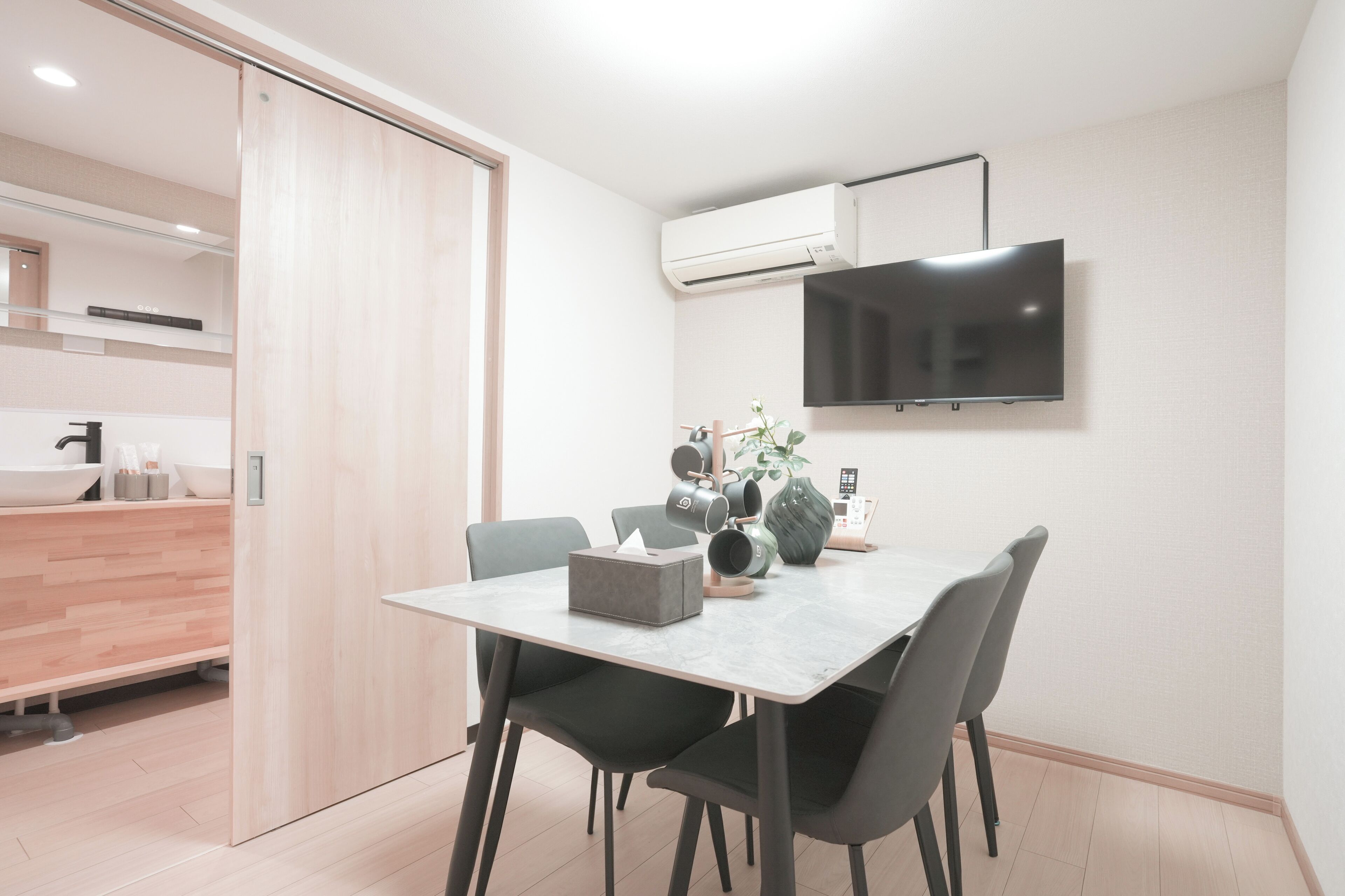 Un comedor moderno con una mesa, sillas, un florero y un televisor montado.