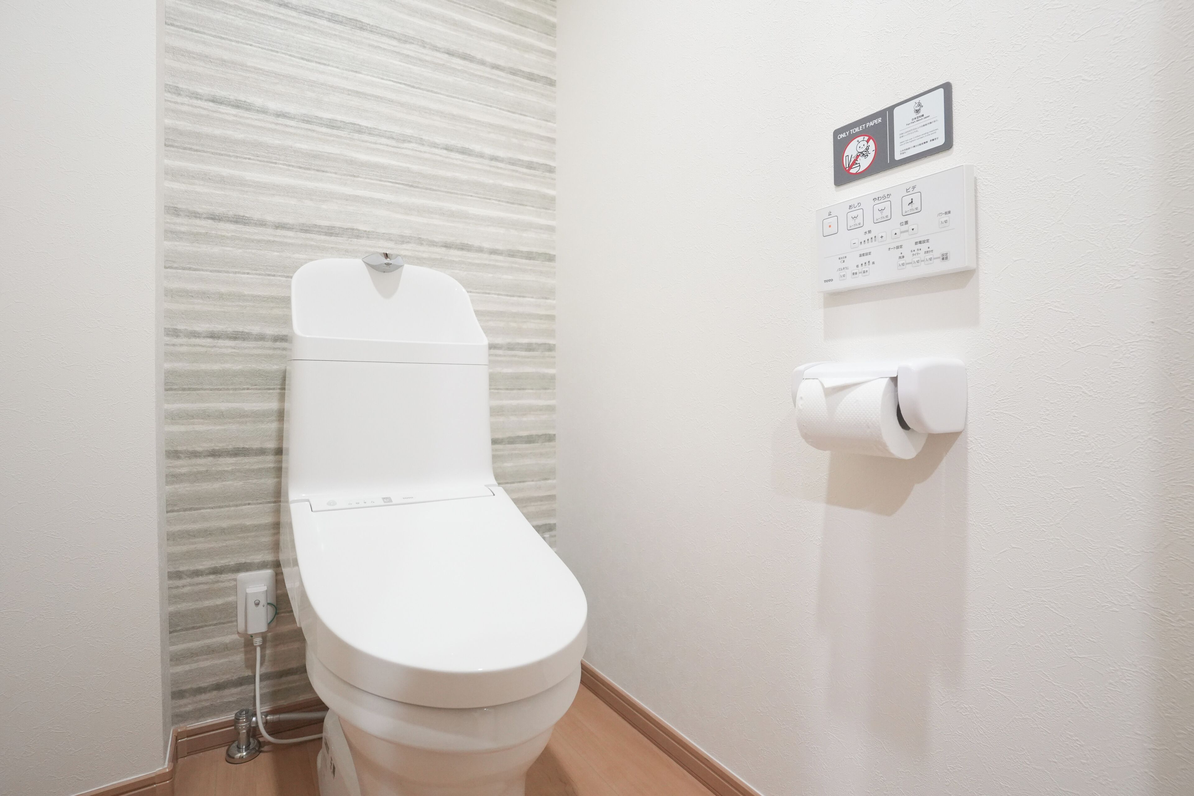 A white toilet with a flush button and a toilet paper holder on the wall.