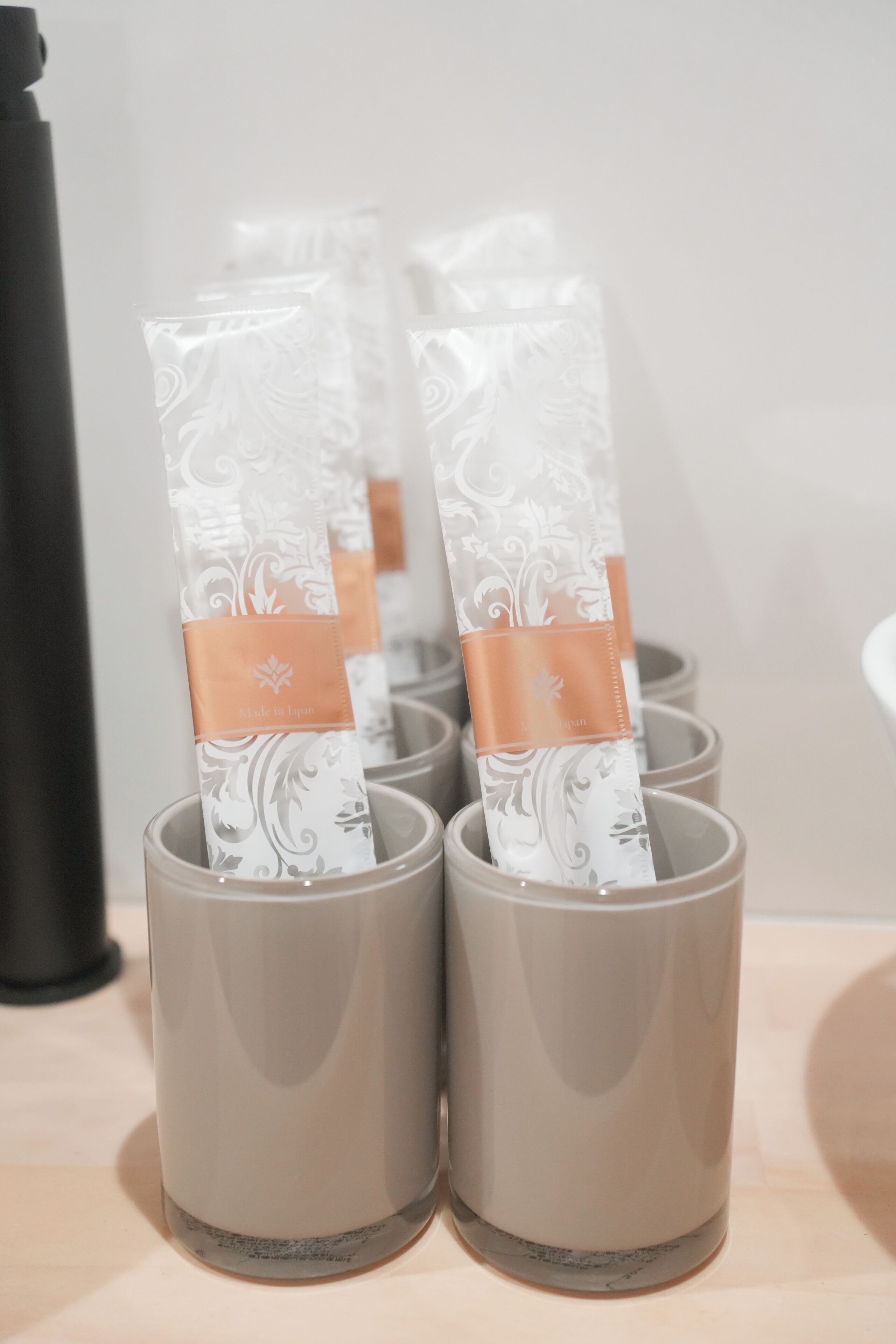 A row of grey cylindrical containers with a white patterned label and a brown band, placed on a flat surface.