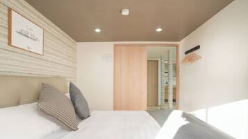 A hotel room with a bed, pillows, a framed picture on the wall, a wooden door, and a coat rack.