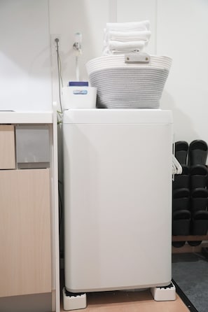 Calentador portátil blanco con panel de control y una toalla doblada encima, sobre un suelo de madera, junto a un armario blanco y un zapatero negro.