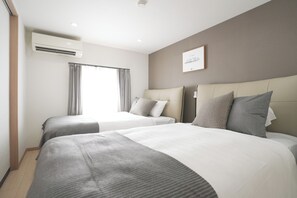 Habitación de hotel con dos camas, una ventana con cortinas, un equipo de aire acondicionado y un cuadro en la pared.