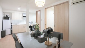 A modern kitchen with white cabinets, a microwave, and a kettle. There is a dining table with chairs, a vase with flowers, and a coffee machine. - b&Tsutenkaku3 (Osaka Naniwa-ku)
