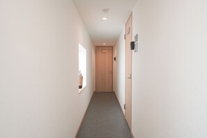 Un pasillo estrecho con una puerta de madera al final, un ventanal pequeño a la izquierda y una lámpara fijada a la pared.