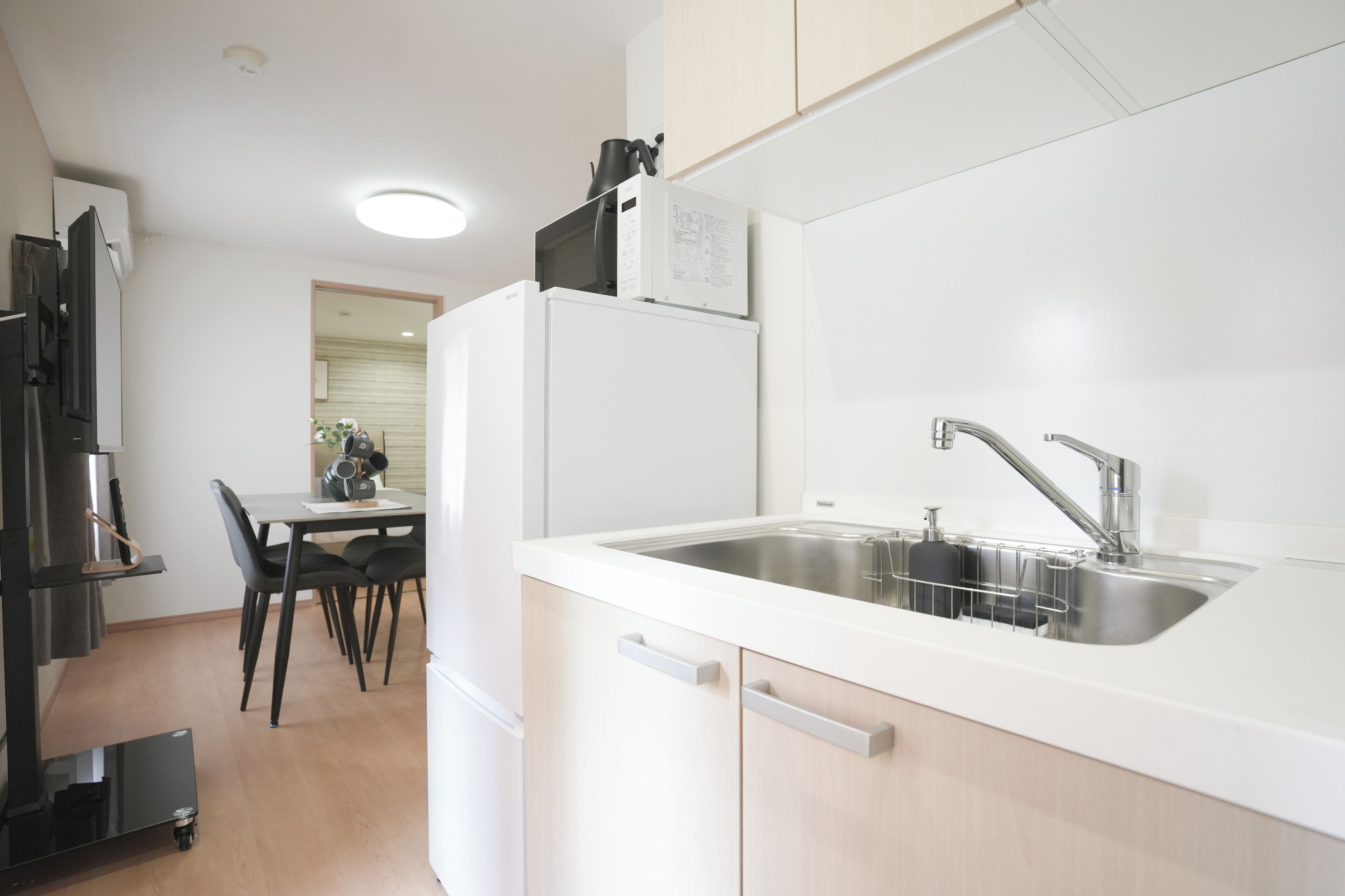 Cocina compacta con pileta integrada, comedor con mesa y sillas, y un refrigerador.