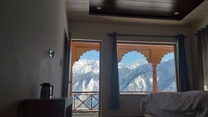 Una habitación con una cama, una ventana que ofrece vistas a montañas nevadas y una cafetera sobre una mesa.