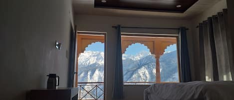 A room with a bed, a window with a view of snow-capped mountains, and a coffee maker on a table.