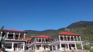Un edificio de varios pisos con balcones, techo rojo y montañas al fondo.