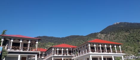 A multi-story building with balconies, a red roof, and a mountainous backdrop.