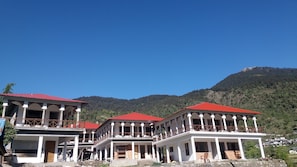 A multi-story building with balconies, a red roof, and a mountainous backdrop. - Dayara Resort (Bhatwari)
