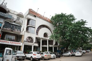 Un edificio de varios pisos con un letrero de hotel visible, una tienda de muebles y coches estacionados a lo largo de la calle.