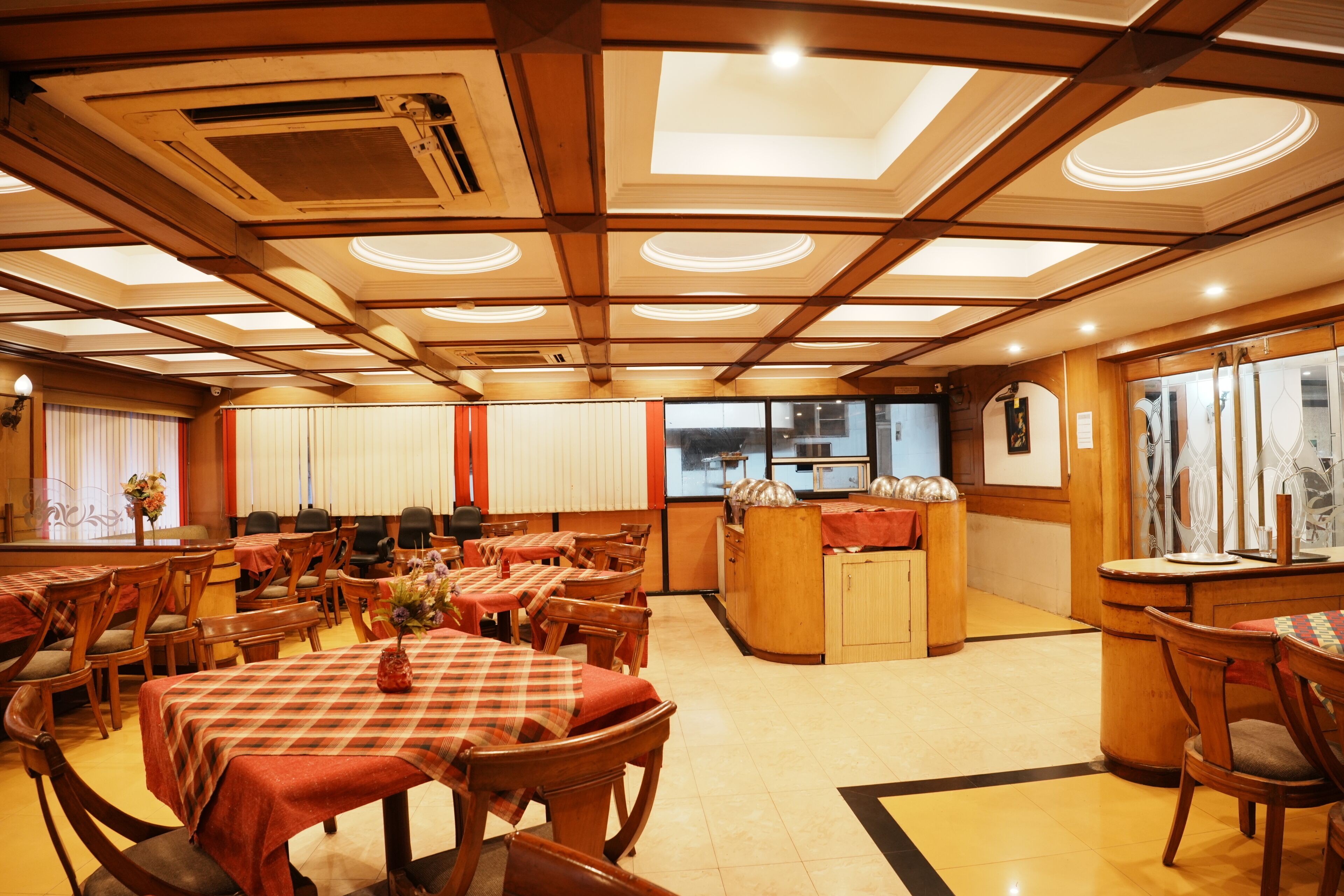 Ein Restaurant mit Holztischen, einer zentralen Bar und einer Decke mit eingelassener Beleuchtung.
