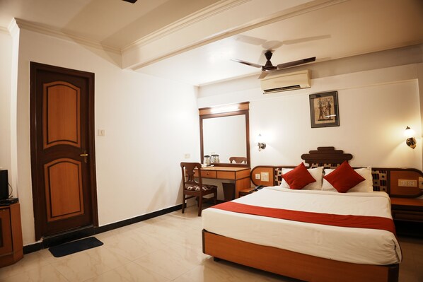 Habitación de hotel con cama, escritorio, silla, armario, puerta y ventilador de techo.