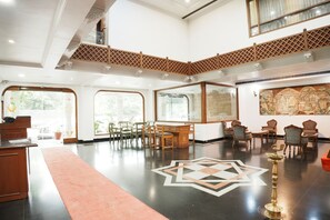 Un hall d’hôtel spacieux avec un plafond haut, un espace de détente central doté de chaises et d’une table, et de grandes fenêtres laissant entrer la lumière naturelle.