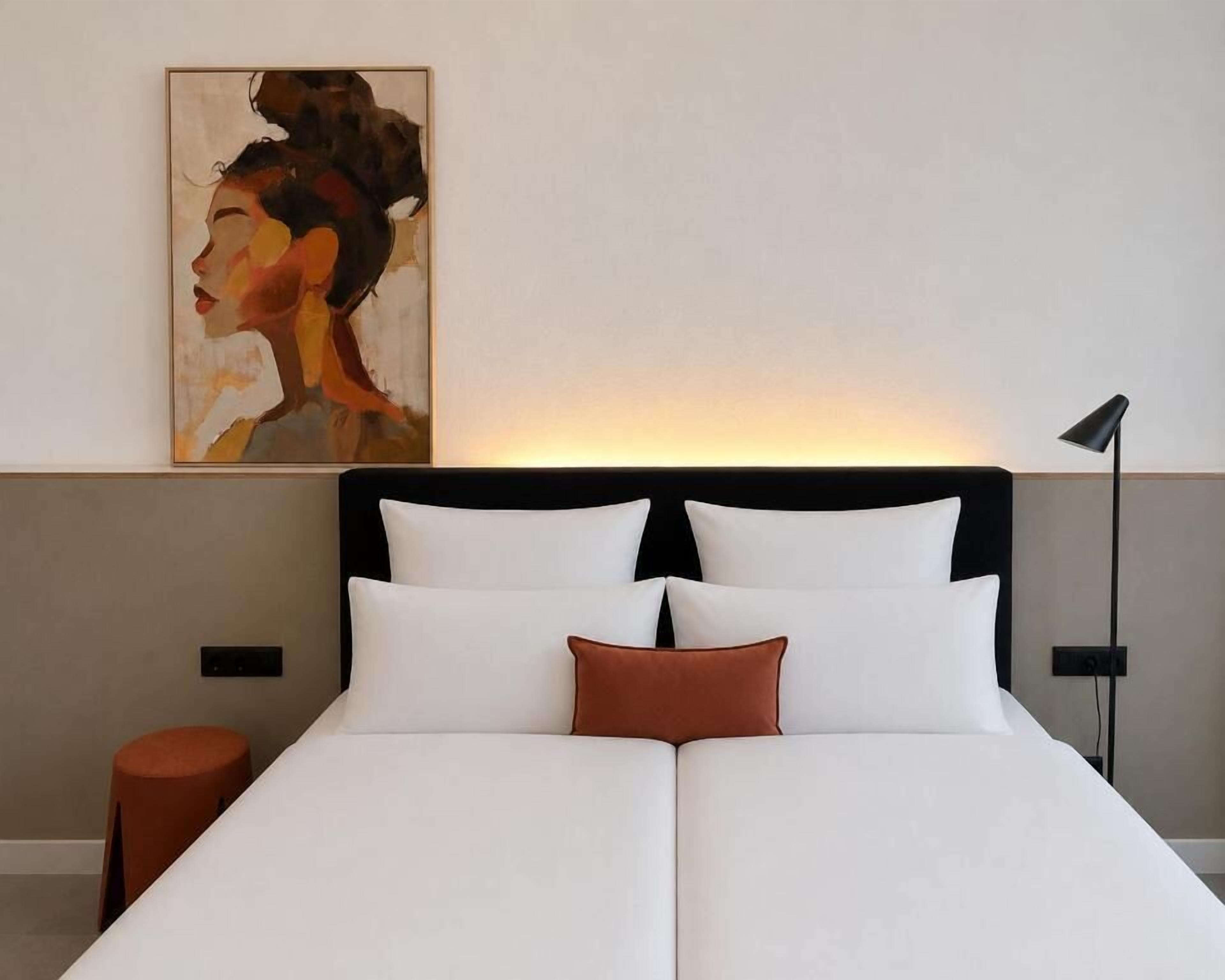 Una habitación de hotel con una cama, un cuadro en la pared, una lámpara de noche y una mesita redonda.