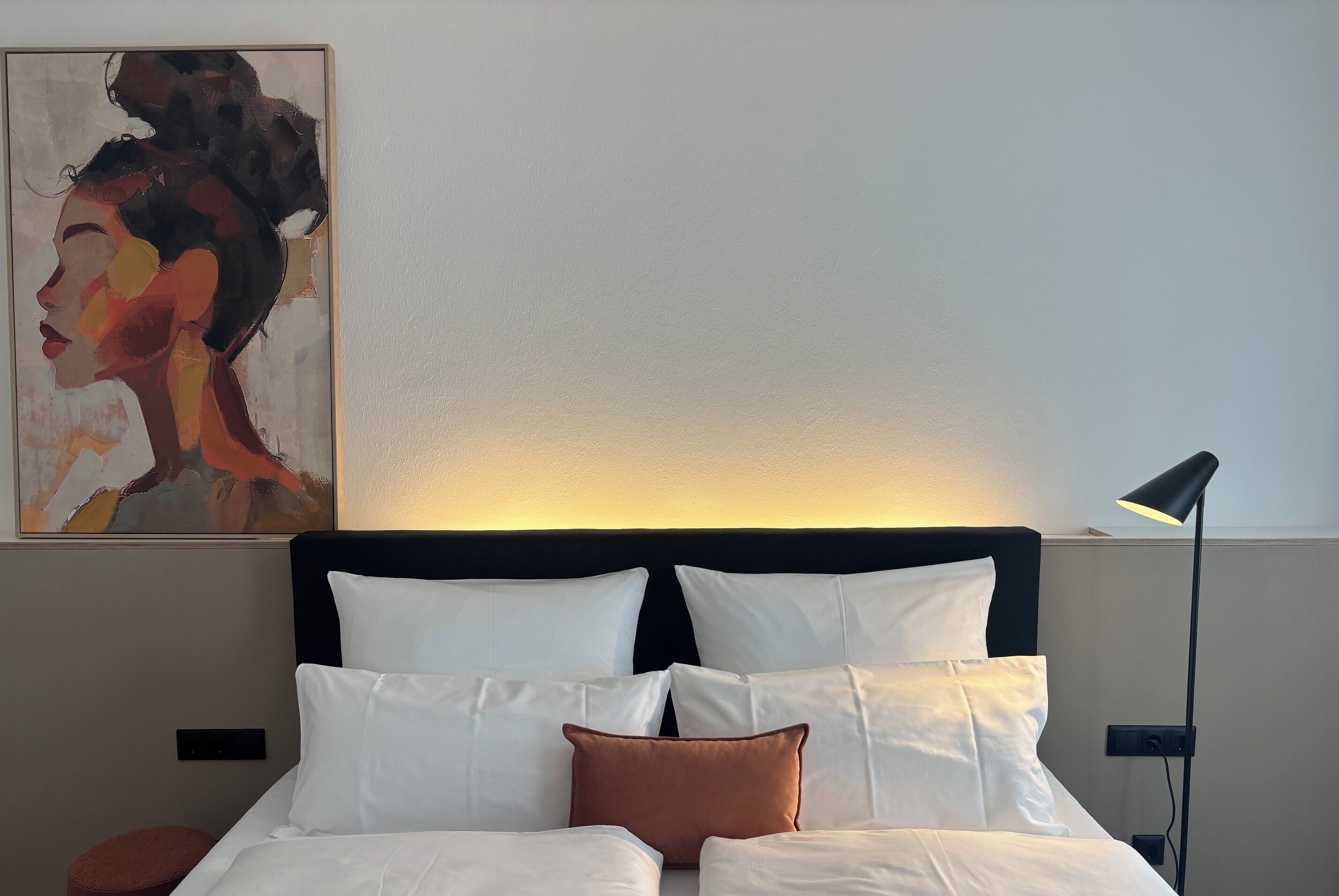 Ein Hotelzimmer mit einem Bett, Kissen, einem Bild an der Wand und einer Stehlampe.